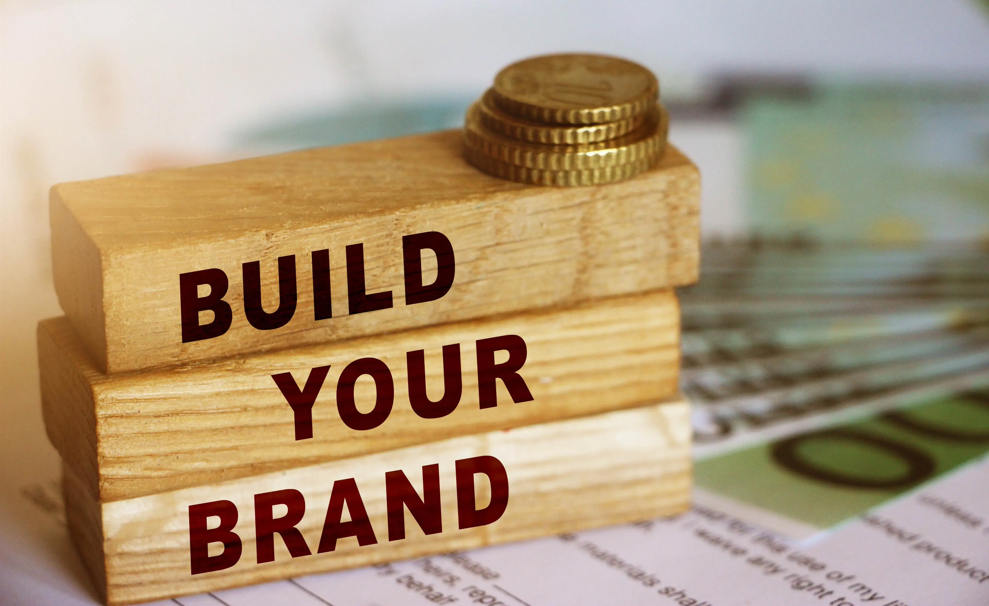 Wooden blocks form the text 'build your brend' on 100 Euro currency bills and coins background. Branding and marketing business concept